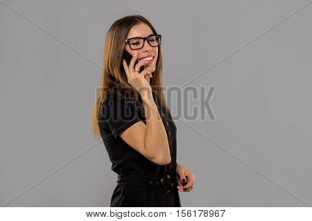 Beautiful brunette woman in glasses talking phono in studio on grey background
