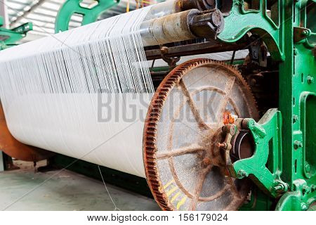 A row of textile looms weaving cotton yarn in a textile mill.