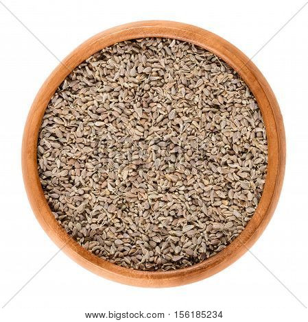 Anise seeds in a wooden bowl on white background. Edible dried fruits of Pimpinella anisum, also called aniseed, with strong sweet flavor. Isolated macro food photo close up from above.
