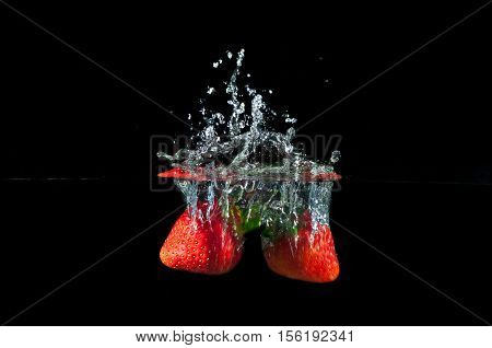 Strawberries splashing into water on a black background