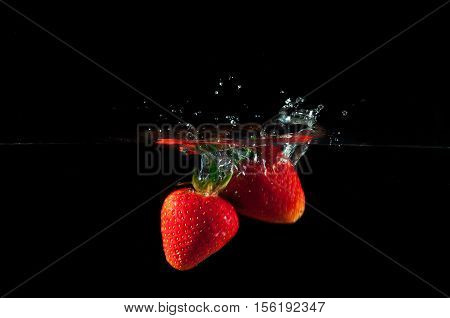 Strawberries splashing into water on a black background