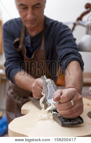artisan lutemaker working a violin in his workshop