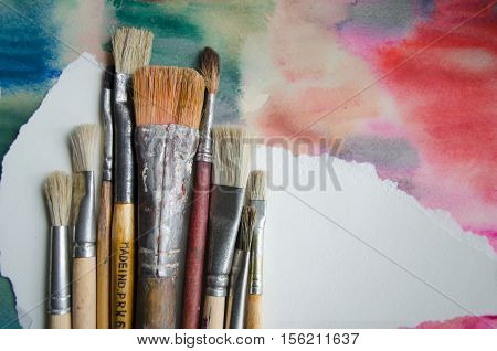 A group of paintbrushes on abstract colorful watercolor background with place for text. Can be used for background banner poster advertising workshops. Blank for motivating quote note message.