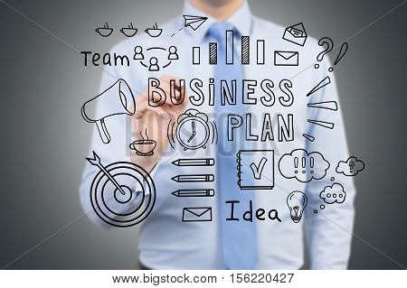 Close up of a man's torso. He is drawing a business plan sketch on glassboard. Black wall is in the background