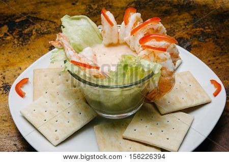Shrimp cocktail with square cookies. Background of wood.