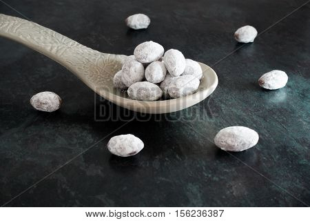 A heap of icing sugar and chocolate coated almonds on a big grey ceramic spoon isolated on black marbled background. Dark food photography selective focus and shallow depth of field.