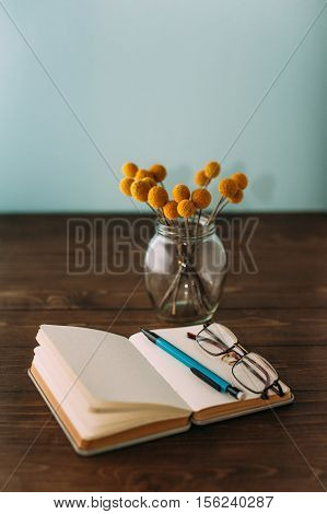 Notebook and flowers Craspedia pen and glasses.