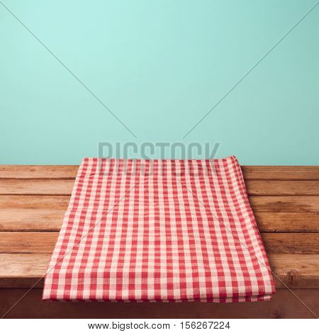 Empty wooden deck table and red checked tablecloth over mint wallpaper background