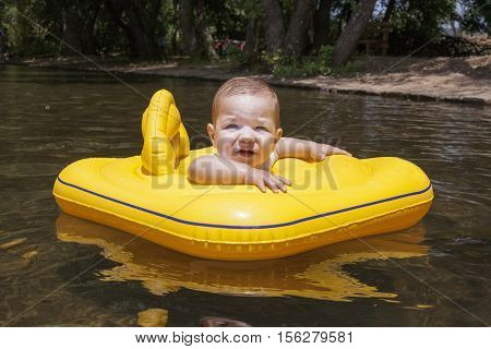 Baby boy with yellow rubber ring on natural river pool