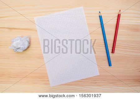 A sheet of paper and pencils on the wooden table. Red and blue pencils. Place for drawing or writing. A blank sheet of paper. Space for text