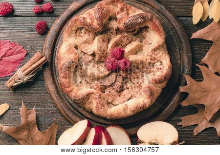 apple pie with cinnamon and raspberry on a wooden table.