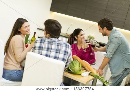 Group of happ young people sitting by the table eating and drinking red wine