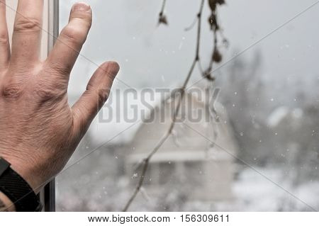 Male hand lean on window looking at the snowfall outsiide, cropped shot with focus in the foreground