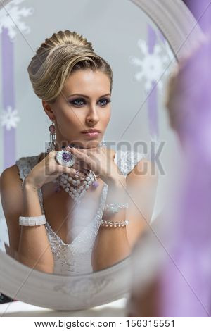 Beautiful young woman with bright purple makeup and fancy hairdo sitting in front of mirror. Gorgeous winter bride.