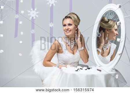 Beautiful young woman with bright purple makeup and fancy hairdo sitting behind mirror table. Gorgeous winter bride. Copy space.