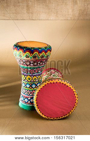 Two decorated colorful pottery goblet drums (chalice drum tarabuka darbuka) on background of wooden table with vanishing shadow lines and sackcloth wall. Low light studio shot