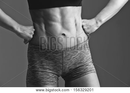 Closeup of fit woman torso with abs muscles. Body part. Fitness. Sudio shot over grey background. Monochrome.