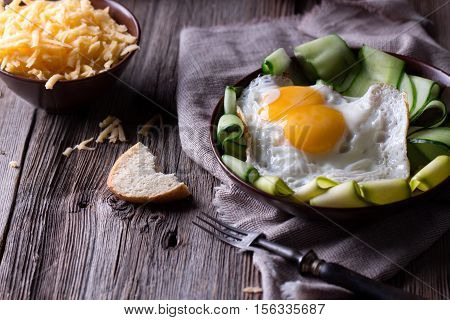 Traditional breakfast. Fried egg with sliced veetables, cheese and bread on old rustic table.
