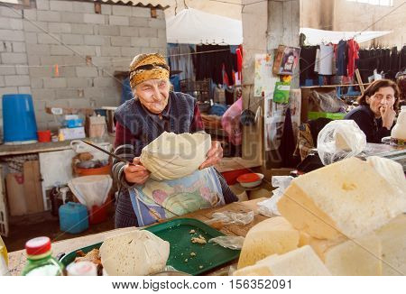 SIGNAGI, GEORGIA - OCT 7, 2016: Senior woman smiling and trading homemade cheese on Georgian rural market on October 7, 2016. Signagi of Kakhetia has a population 2.200