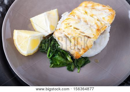 Fried cod fillets spinach and lemon on the plate