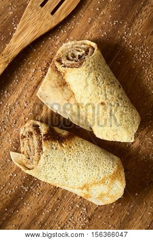 Crepe rolls filled with cinnamon and sugar photographed overhead on wood with natural light (Selective Focus Focus on the top of the rolls)