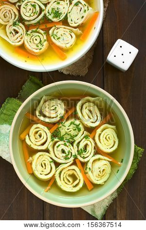 Traditional German Flaedlesuppe and Austrian Frittatensuppe based on consomme with rolls or stripes of pancake or crepe garnished with chives photographed overhead on wood with natural light (Selective Focus Focus on the soups)