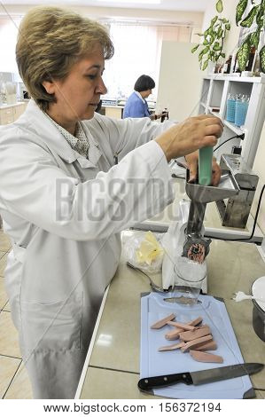 Saint-Petersburg Russia - July 8 2013: National Centre for the control and quality of goods and services. Chemical laboratory for testing food. Woman chemist technician examines the quality of cooked sausage