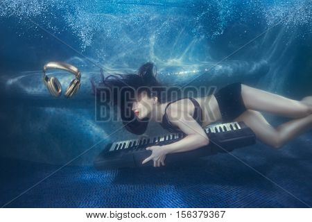 Girl swims with piano under water in the pool.