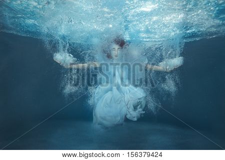 Girl under water in the pool among the splash of water and bubbles.