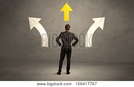 A confused businessman facing a grey urban wall with a yellow arrow pointing in the right direction concept