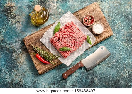 Raw minced meat with olive oil and seasoning on paper over blue stone background. top view with copy space.