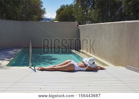 female in a swimsuit lying near the pool with hat and wine