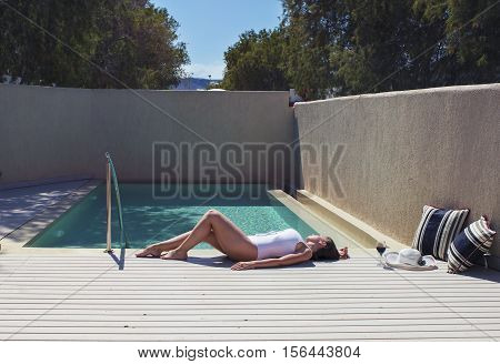female in a swimsuit lying near the pool with hat and wine