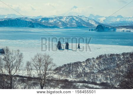 Three rocks in the sea among the ice - Three Brothers against the backdrop of the volcano Viluchinsky the Kamchatka Peninsula. Toned horizontal image.