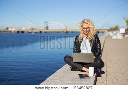 Busy hippster sitting by the water and working on computer