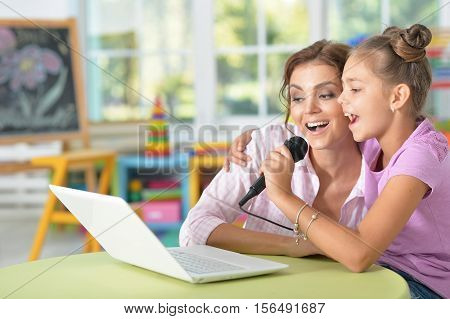 Young mother and her cute daughter singing karaoke at home