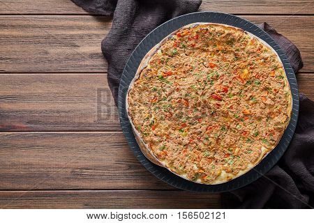 Lahmacun homemade turkish delicious dough pizza with minced beef or lamb meat, paprika, tomatoes, cumin spice, parsley baked spicy middle eastern arabian food on rustic wooden table background