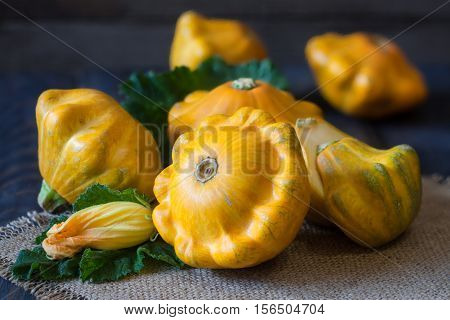 three yellow pattypan squash with leaf and flower on a dark wooden table.