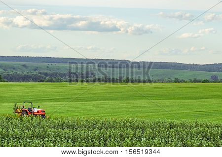 Small red farm tractor on a background of green meadows. Agricultural background with copy space.