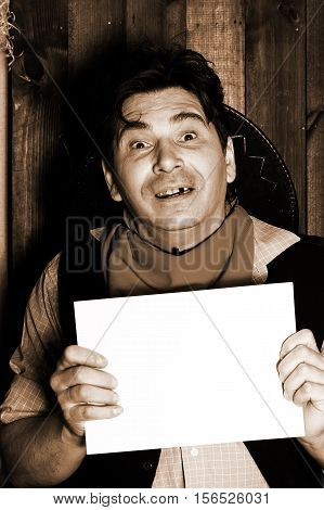 Portrait of a wanted cowboy man holding a sign in her hand with empty space for text. Man looking at the camera toothless smile without a hat. Background in grunge style.