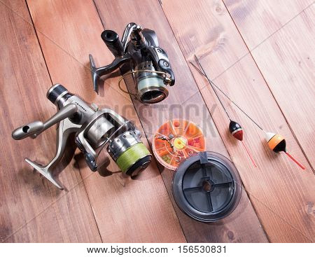 Fishing accessories reel spools of fishing line floats and a box of hooks on wooden background