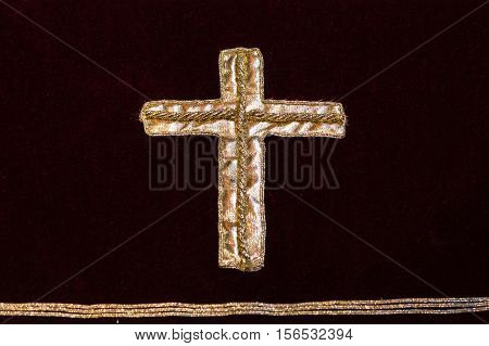 A gold cross embroidered on a dark red cloth