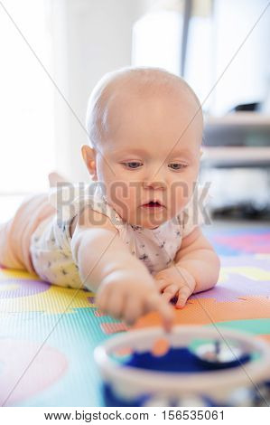 Baby girl with blue eyes playing on the floor with toys on a playmat. A cute young child plays.