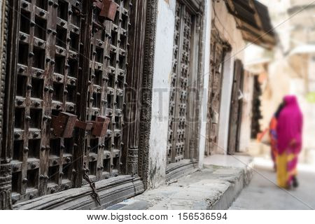 typical Zanzibar town street with old iron doors and wooman walking away, Africa