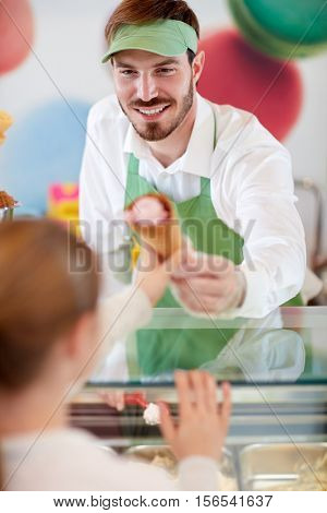 Kind male seller in candy store gives ice cream to girl