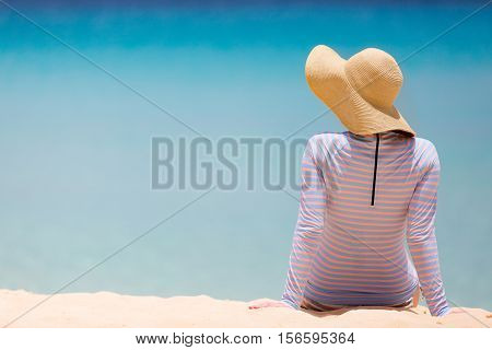 back view at young woman at the beach in sunhat and rashguard or swimsuit enjoying perfect caribbean sea sun protection concept