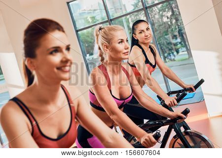 Young women exercising on stationary bicycles in fitness gym. focus on the girl away