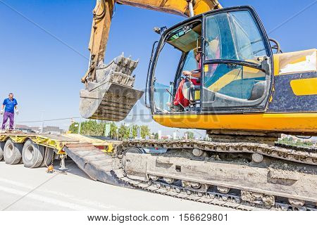 Zrenjanin Vojvodina Serbia - August 27 2015: Heavy excavator it climbs on low platform trailer over back ramp carrying two buckets inserted into one another.