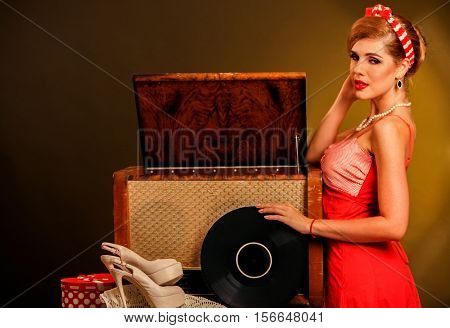 Girl in style keeps vinyl record. Pin-up retro female style. Girl pin-up style wearing red dress. Girl is going to listen to music in Christmas evening.