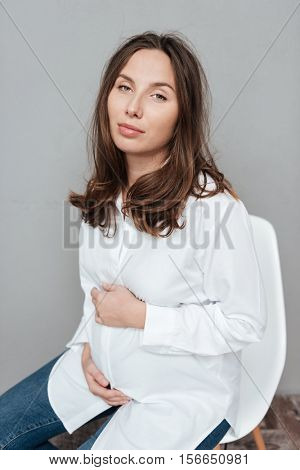 Fashion pregnant woman in studio. ssitting on a chair. isolated gray background